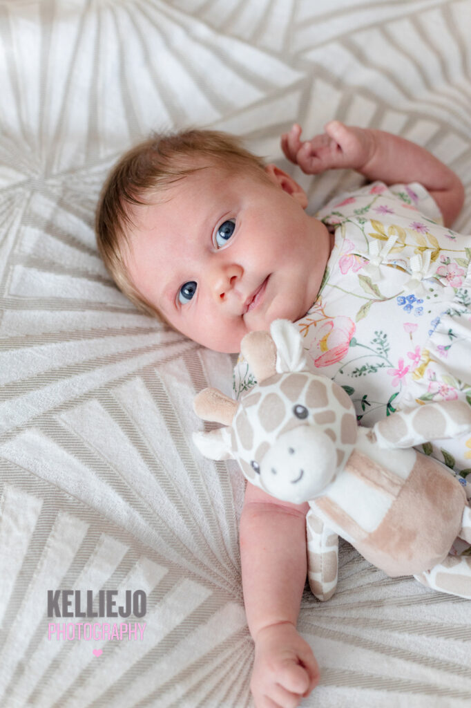 newborn baby with her toy giraffe laying on a bed during a newborn photoshoot in Manchester
